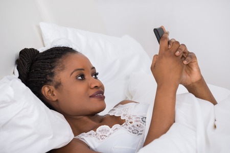Start every morning with a spring in your step - Morning Routine (50245438 - young african woman lying on bed using mobile phone)