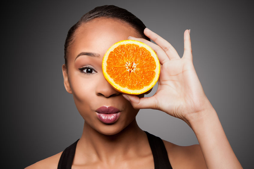 How a Vitamin C boost can be just what your skin needs this winter 74368223 - beautiful healthy happy black asian woman holding delicious orange mandarin fruit in front of eye.