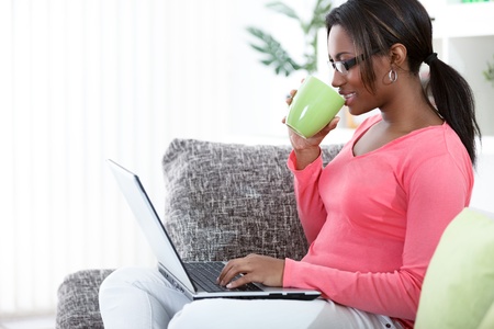 19404905 - black woman using a laptop while having a tea in her living room Refresh your life with a good spring clean