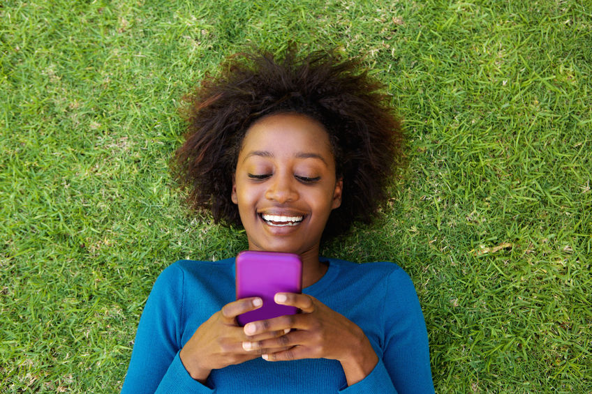 53357923 - portrait from above of a smiling african woman lying on grass looking at cell phone 8 Essential apps for a healthy and happy life