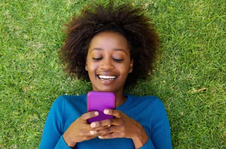 53357923 - portrait from above of a smiling african woman lying on grass looking at cell phone 8 Essential apps for a healthy and happy life
