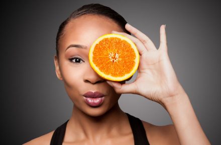 How a Vitamin C boost can be just what your skin needs this winter 74368223 - beautiful healthy happy black asian woman holding delicious orange mandarin fruit in front of eye.